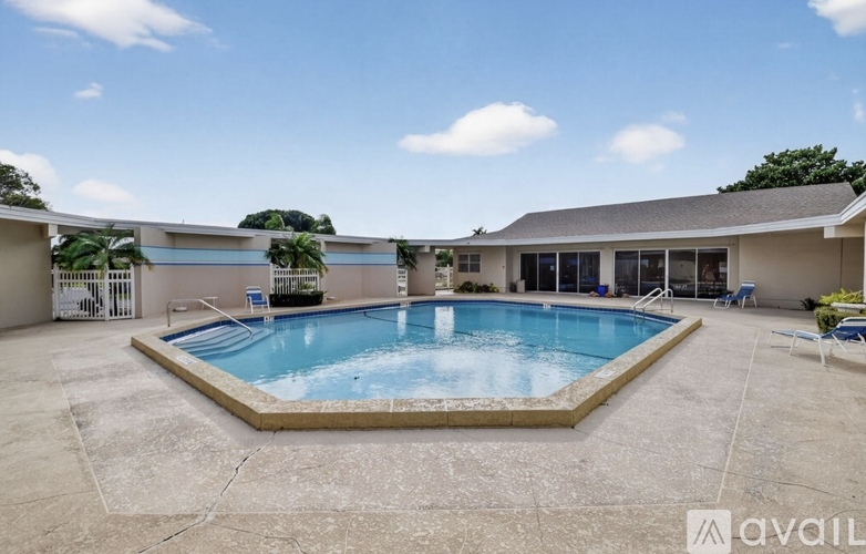 A large outdoor swimming pool is surrounded by a concrete patio and a covered area with lounge chairs.