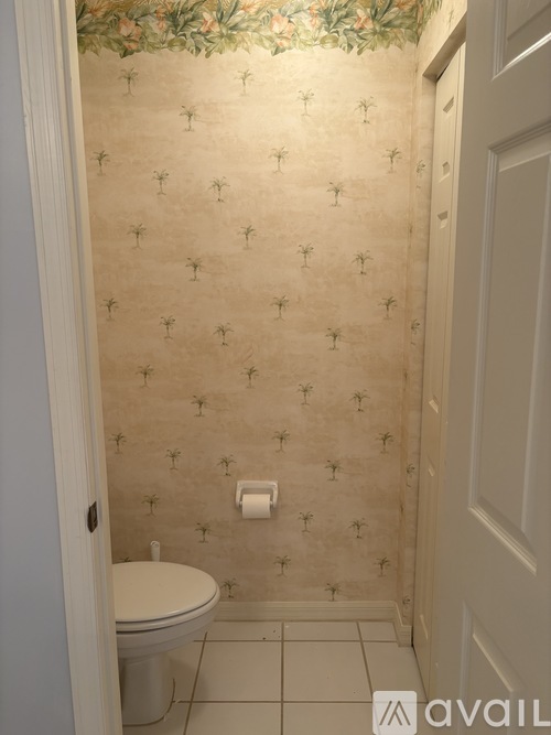 A bathroom with a toilet and wallpaper with a pattern of palm trees.