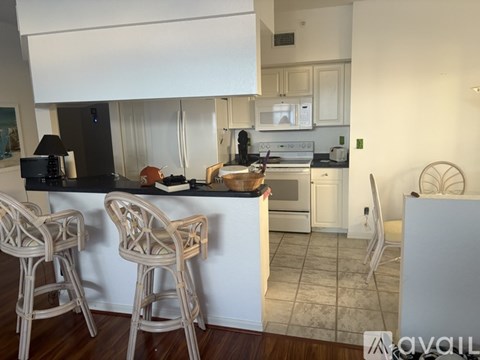 A kitchen with white cabinets and a black countertop with two barstools in front.