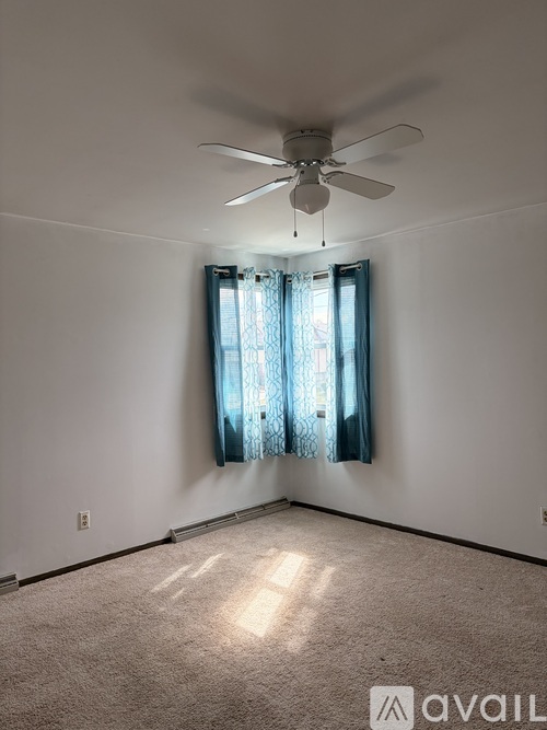 A room with a ceiling fan and a window with curtains.