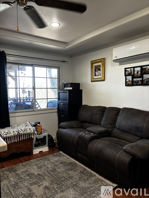 A living room with a black leather sofa and a ceiling fan.