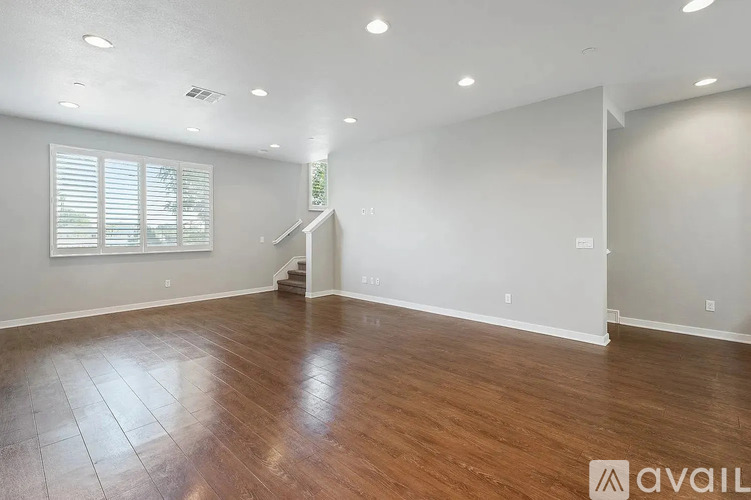 A spacious room with wooden flooring and a staircase in the background.