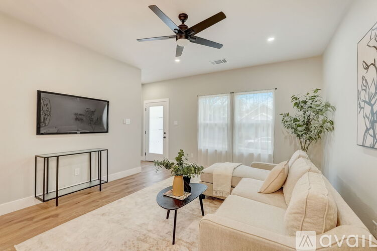 A living room with a beige couch, a black coffee table, and a flat-screen TV mounted on the wall.