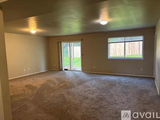 A spacious room with a carpeted floor, a ceiling light, and a sliding glass door leading to a backyard.