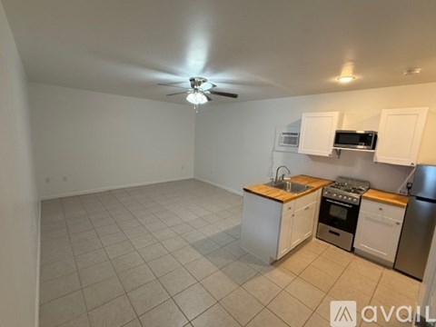 A kitchen with white cabinets and appliances, a ceiling fan, and a tiled floor.