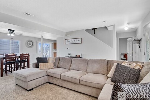 A living room with a beige couch and a clock on the wall.
