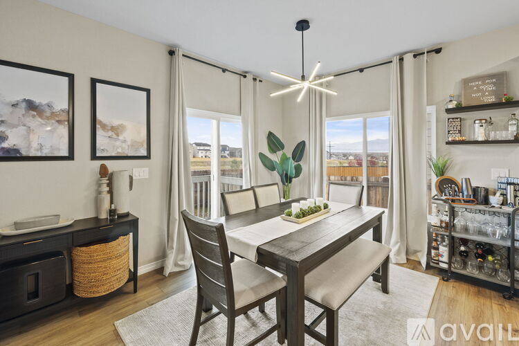 A dining room with a wooden table and chairs, a potted plant, and a kitchen area in the background.