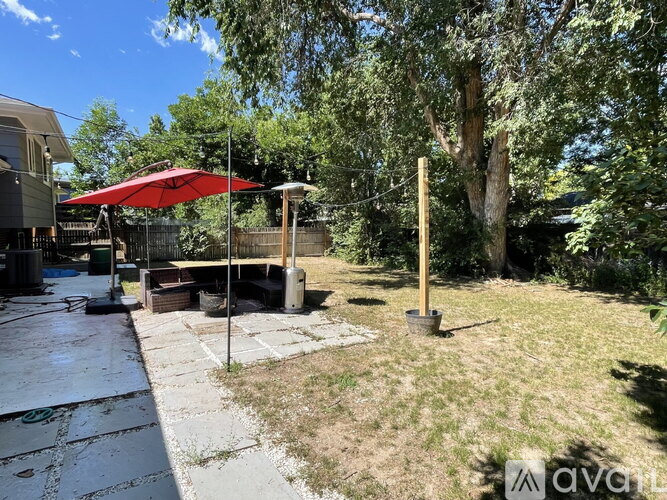 A patio with a red umbrella and a table surrounded by trees.