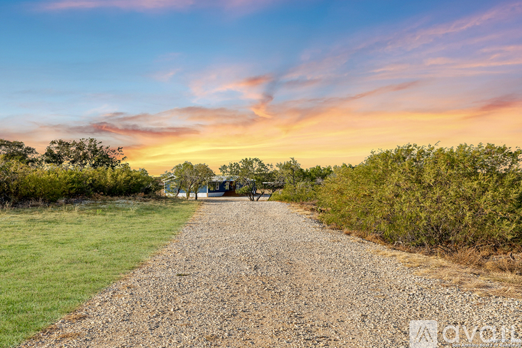 A gravel path leads through a grassy area with a house in the distance.