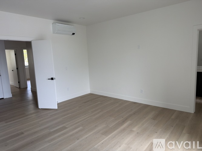 A spacious room with wooden flooring and a white wall.
