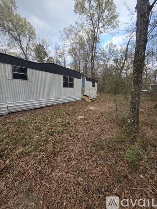 A metal building with a black roof is surrounded by trees and grass.