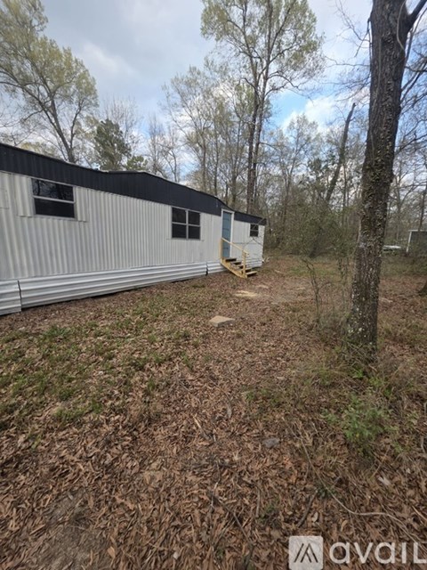 A metal building with a black roof is surrounded by trees and grass.