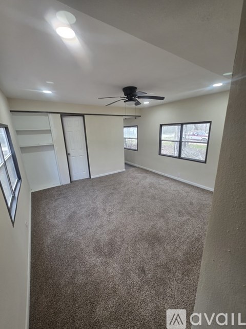 A room with a carpeted floor, a ceiling fan, and a window with blinds.