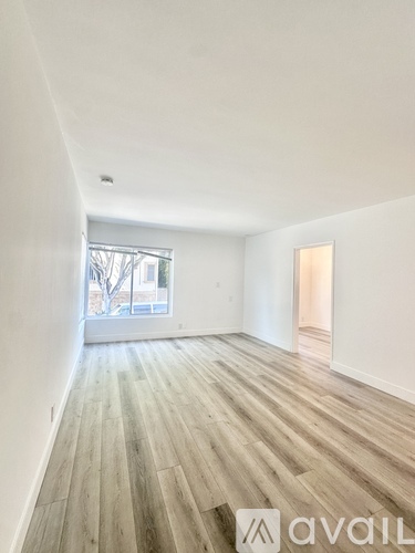 A room with wooden flooring and white walls, with a window and a door visible.