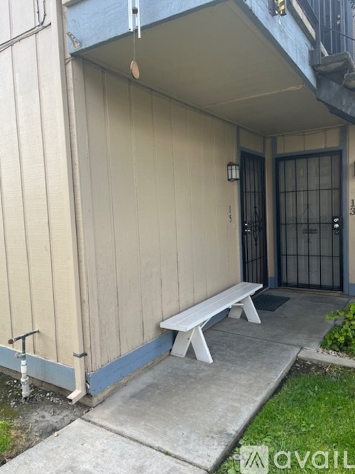 A white bench is outside a building with a black gate.