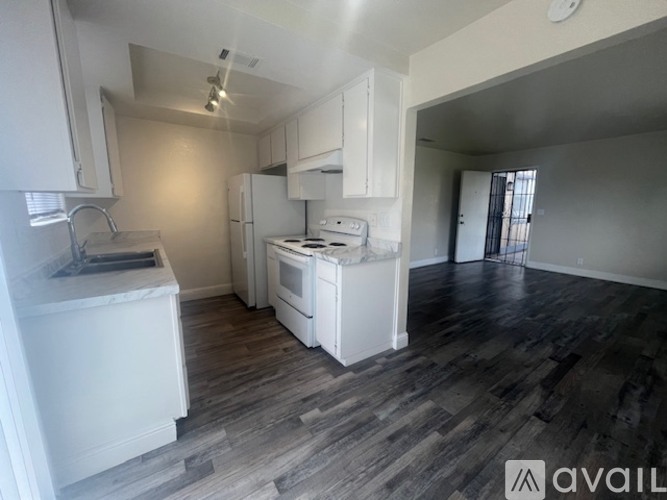 A kitchen with white appliances and cabinets, and a wooden floor.