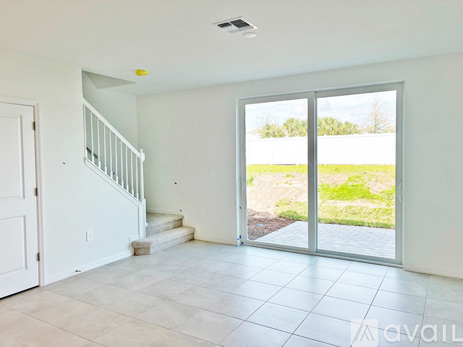 A spacious room with a staircase and sliding glass doors leading to a backyard.