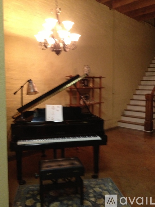 A black piano with a white label on it is in a room with a staircase in the background.
