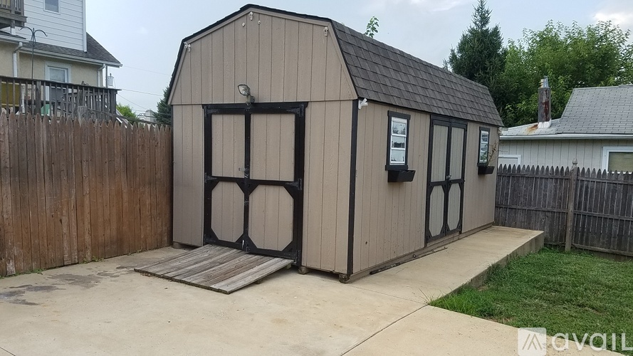 A small brown building with a black door and windows is situated in a driveway.