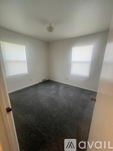 A room with a carpeted floor and two windows.