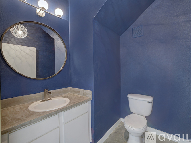 A bathroom with blue walls, a white toilet, and a round mirror.