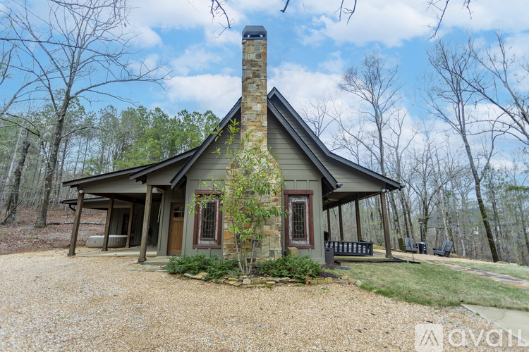 A small house with a stone chimney is surrounded by trees.