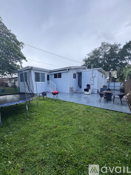 A backyard with a trampoline and a white house.