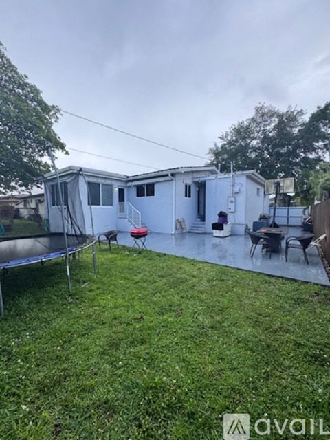 A backyard with a trampoline and a white house.