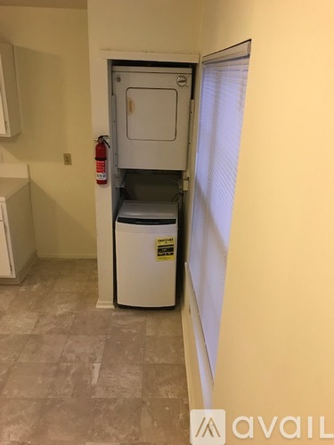 A small white refrigerator with a black sticker on it is in a corner of a room with a fire extinguisher on the wall.