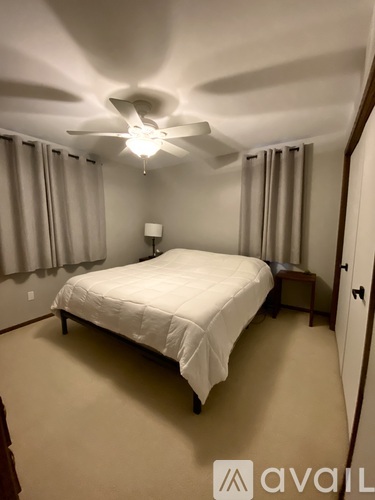 A bedroom with a bed, nightstand, and window with curtains.