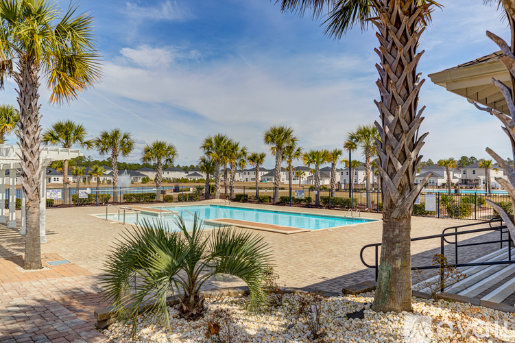 A pool surrounded by palm trees and a building in the background.