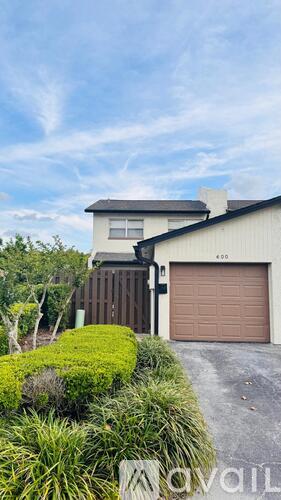 A house with a brown garage door is surrounded by greenery.