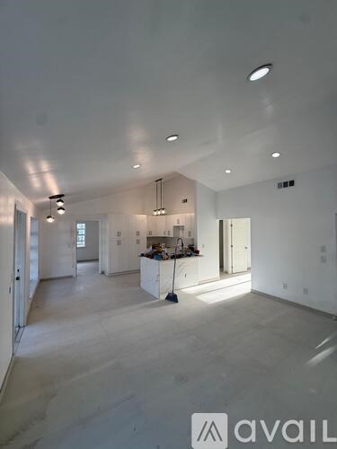 A white interior space with a kitchen area and a vacuum cleaner.
