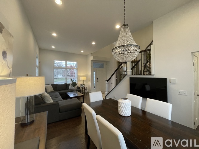 A modern living room with a grey sofa, a wooden dining table, and a chandelier hanging from the ceiling.
