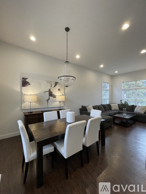 A modern dining room with a dark wood table and white chairs.