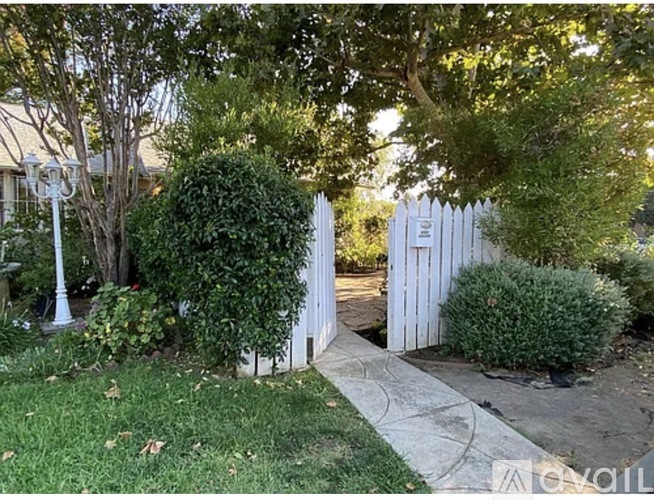 A white picket fence with a gate in the middle of a garden.