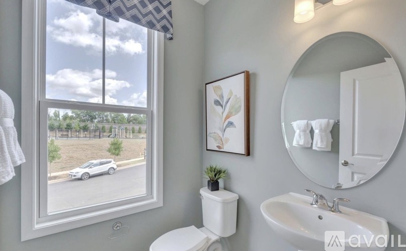 A bathroom with a toilet, sink, mirror, and a window with a view of a car and trees.