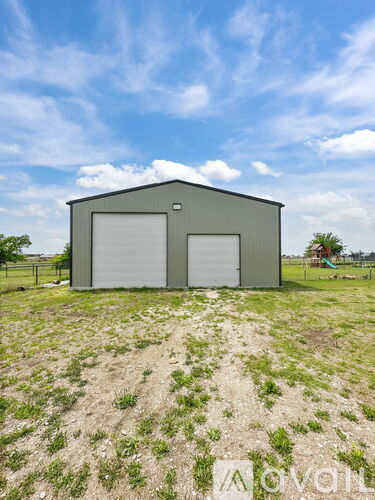 A grey metal building with two white garage doors stands in a field.