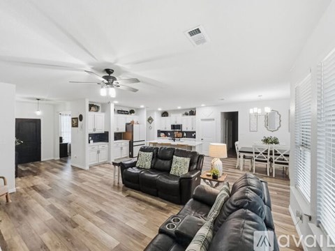 A living room with a black leather couch and wooden floors.