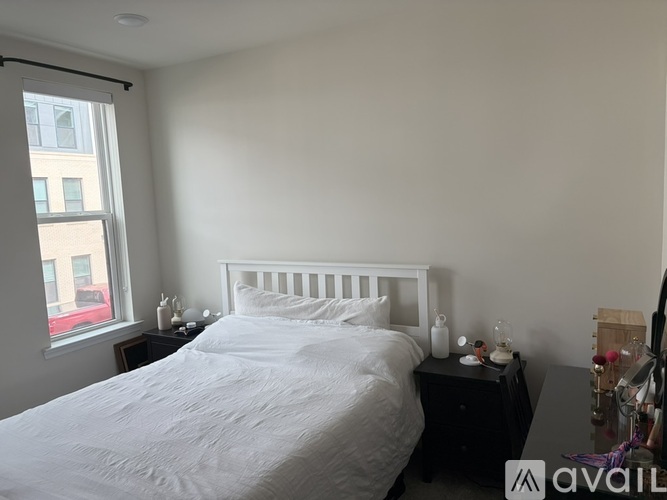 A bedroom with a white bed and a window with a view of a city.