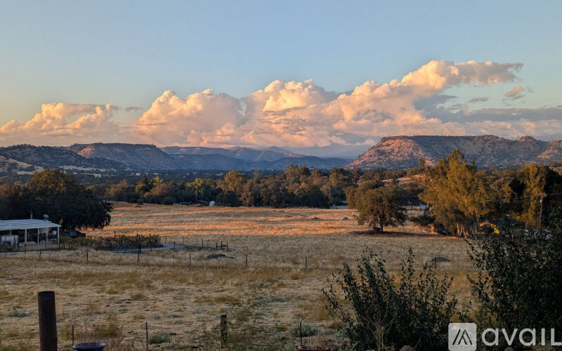A landscape with a house, fence, and trees with mountains in the background.