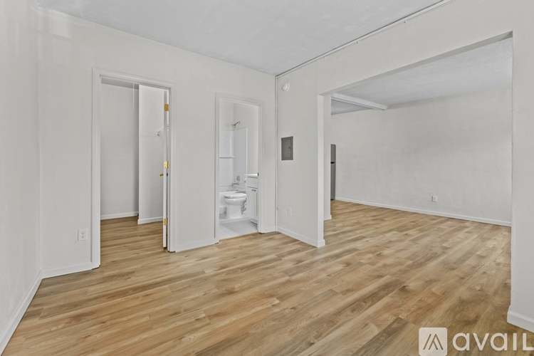A room with wooden floors and white walls, with a doorway leading to another room.