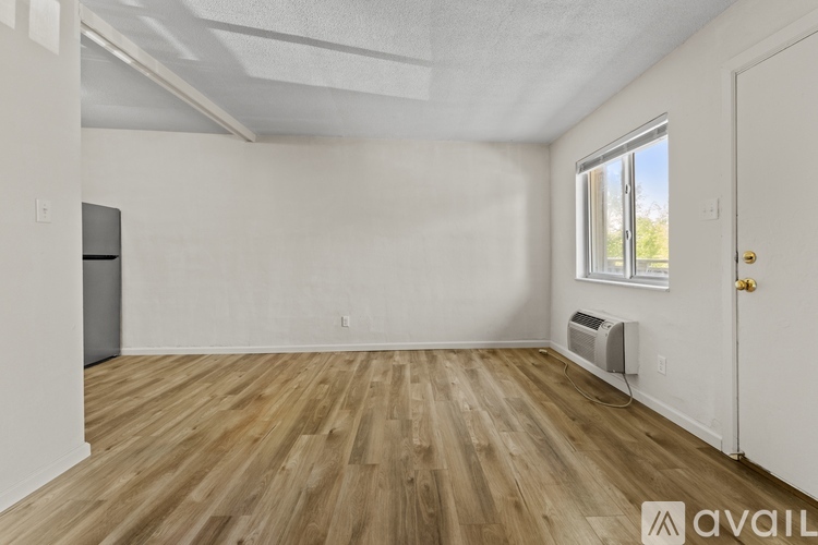 A room with wooden flooring and white walls, with a window and a door visible.