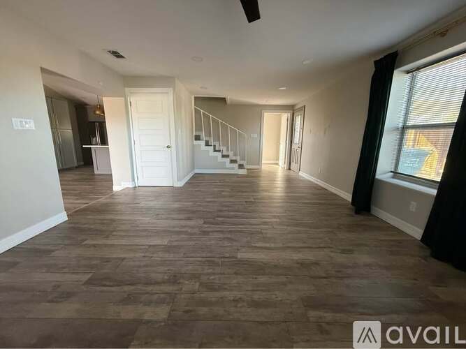 A spacious room with wooden flooring and a staircase in the background.