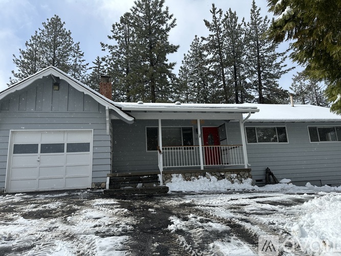 A house with a red door and a garage door is surrounded by snow.