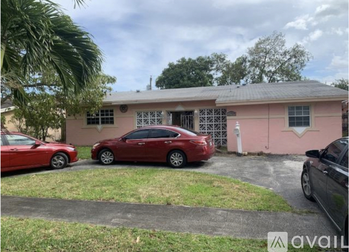A red car is parked in front of a pink building.
