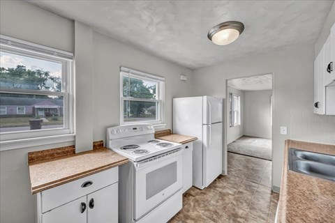 A kitchen with white appliances and a window overlooking a house.