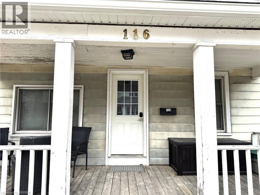 A white house with a black bench and chair on the porch.