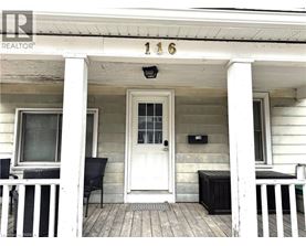 A white house with a black bench and chair on the porch.