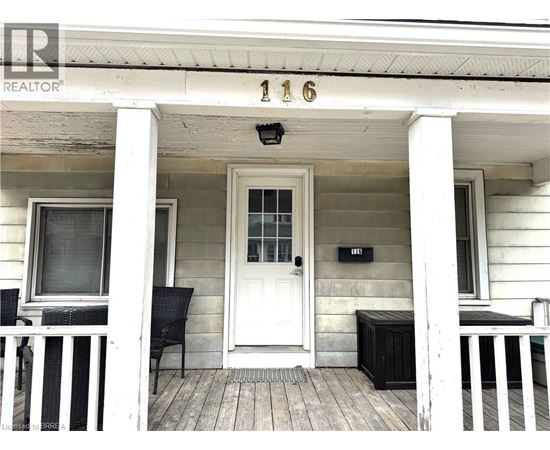 A white house with a black bench and chair on the porch.